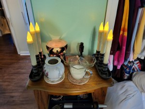 A shrine with candles, a small statue of Ra, and glassware.
